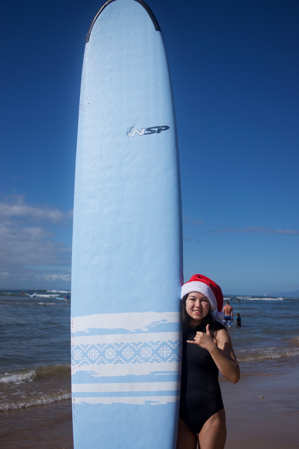 Teenage girl in a Santa hat holding a large surfboard at the beach